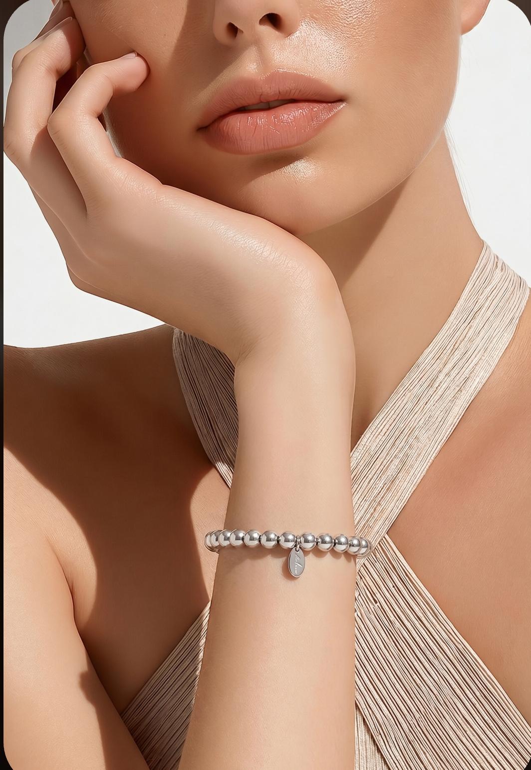 Model draagt massieve zilveren kralenarmband aan de pols, close-up met hand tegen wang