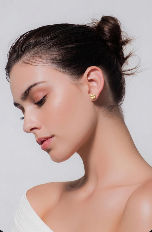 Model draagt gouden klavertje vier oorknopje aan het oor, elegant zijaanzicht met opgestoken haar